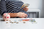Symbolbild einer schwangeren Frau mit Sparschwein und Geld