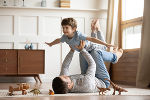 Ein Vater liegt mit dem Rücken am Boden und hält seinen Sohn in Fliegerposition. Ein Vater liegt mit dem Rücken am Boden und hält seinen Sohn in Fliegerposition.