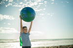 Kind steht am Strand und hält einen Wasserball in der Form der Erdkugel in die Höhe. Kind steht am Strand und hält einen Wasserball in der Form der Erdkugel in die Höhe.