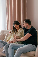 Ein paar sitzt auf einer Couch, die Frau ist schwanger und der Mann legt einen Arm um die Frau und den anderen auf den Babybauch. Ein paar sitzt auf einer Couch, die Frau ist schwanger und der Mann legt einen Arm um die Frau und den anderen auf den Babybauch.
