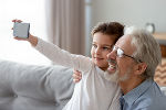 Ein Kind sitzt mit einem Großvater auf der Couch und sie machen ein Selfie. 