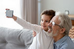 Opa sitzt mit seinem Enkelsohn auf der Couch und beide lächeln ins Handy. Opa sitzt mit seinem Enkelsohn auf der Couch und beide lächeln ins Handy.