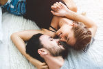 Ein Mann und eine Frau liegen mit am Boden, den Kopf zu einander gedreht und umarmen sich zärtlich. 