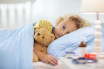 Krankes Kind liegt mit Stofftier im Bett
